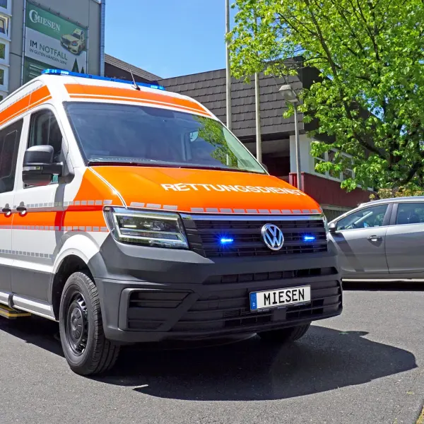 KTW auf VW Crafter-Basis mit orangener RETTUNGSDIENST-Beklebung und Blaulichtanlage, aufgenommen vor dem Gebäude der Firma Miesen.