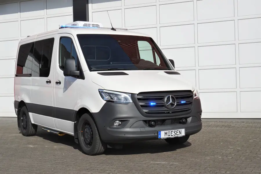 Weißer Mercedes-Benz Sprinter mit eingeschalteter blauer LED-Signalanlage vor einer Garagenwand.