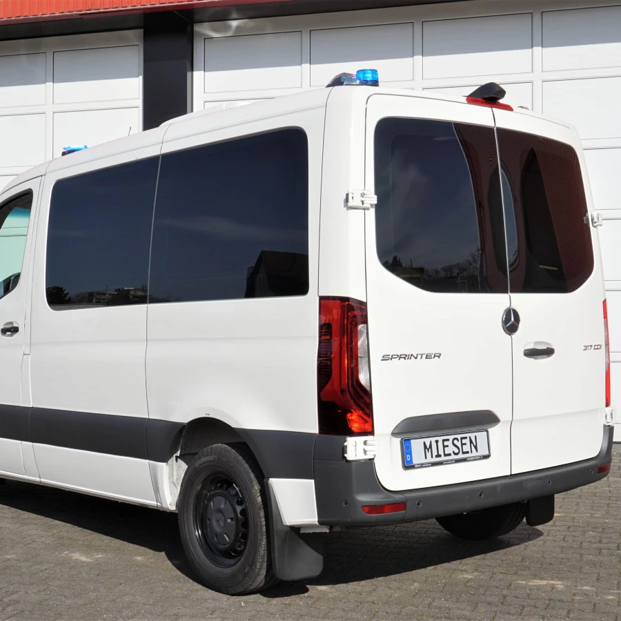 Weißer Mercedes-Benz Sprinter mit blauer Signalleuchte auf dem Dach, abgestellt vor einem Garagentor.