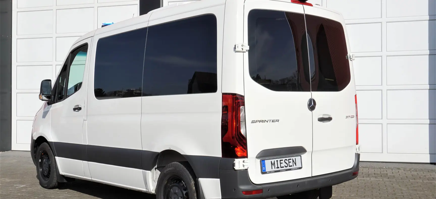 Weißer Mercedes-Benz Sprinter mit MIESEN-Kennzeichen, geparkt vor einer modernen Garagenfront.