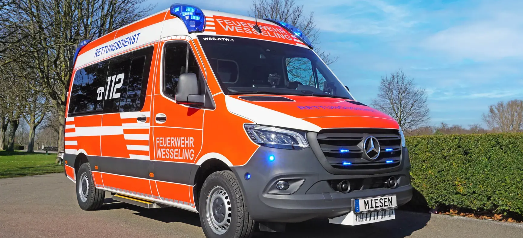 Rettungswagen der Feuerwehr Wesseling auf Mercedes-Benz Sprinter mit eingeschaltetem Blaulicht im Freien.