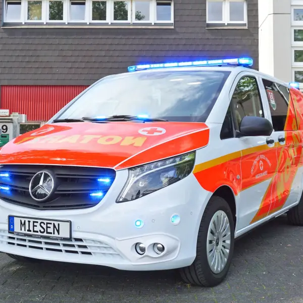 NEF mit roter Beklebung und Blaulicht vor Firmengebäude.