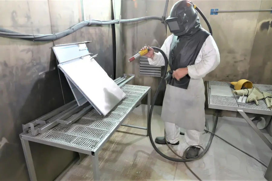 Arbeiter beim Sandstrahlen eines Metallteils in Schutzkleidung