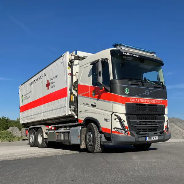 Lastwagen des Katastrophenschutzes mit Anhänger des Deutschen Roten Kreuzes auf einer Straße, zwei Einsatzkräfte im Vordergrund.