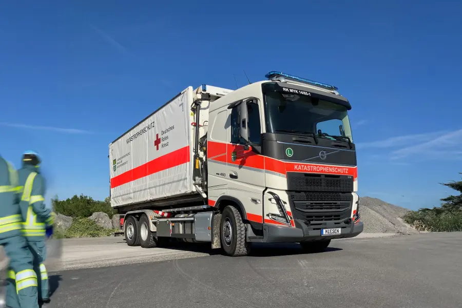 Lastwagen des Katastrophenschutzes mit Anhänger des Deutschen Roten Kreuzes auf einer Straße, zwei Einsatzkräfte im Vordergrund.