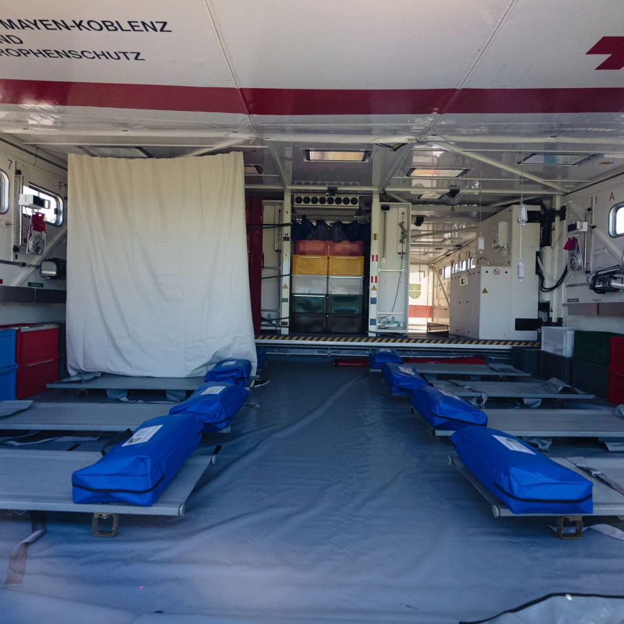 Innenansicht eines Katastrophenschutz-Containers des Deutschen Roten Kreuzes mit vorbereiteten Liegen und farblich sortierten Aufbewahrungsboxen.