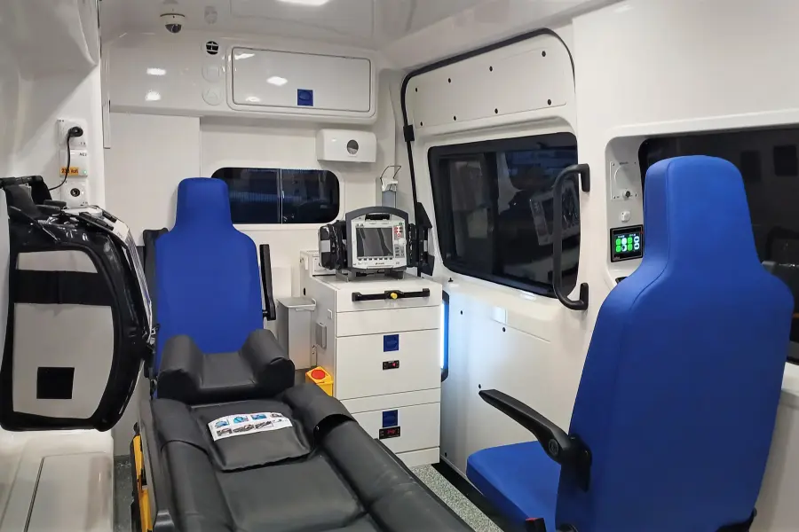 Innenraum eines Rettungswagens mit Trage, blauen Sitzen und medizinischer Ausstattung wie Defibrillator und Notfalltasche.