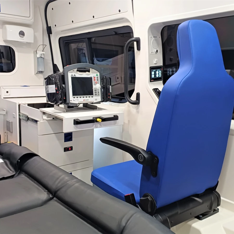 Innenraum eines modernen Rettungswagens mit Trage, zwei blauen Sitzen und medizinischem Monitorgerät.