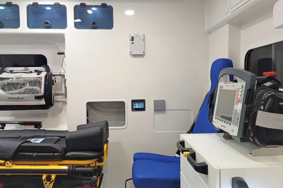 Innenansicht eines Rettungswagens mit Trage, Beatmungsgerät und Defibrillator auf weißem Schrank.
