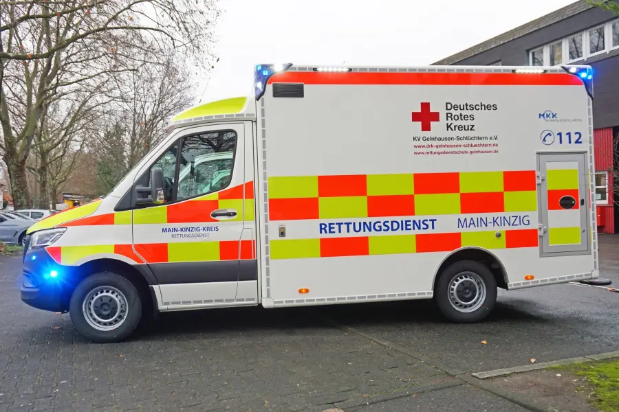 Rettungswagen des DRK Main-Kinzig-Kreis mit Warnbeklebung und aktiver Blaulichtanlage in Seitenansicht.