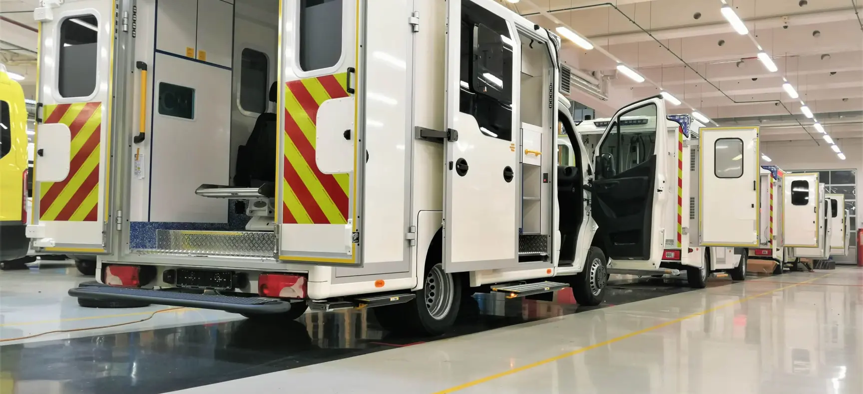 Mehrere Rettungsfahrzeuge in einer Produktionshalle mit geöffneten Türen während des Ausbaus.