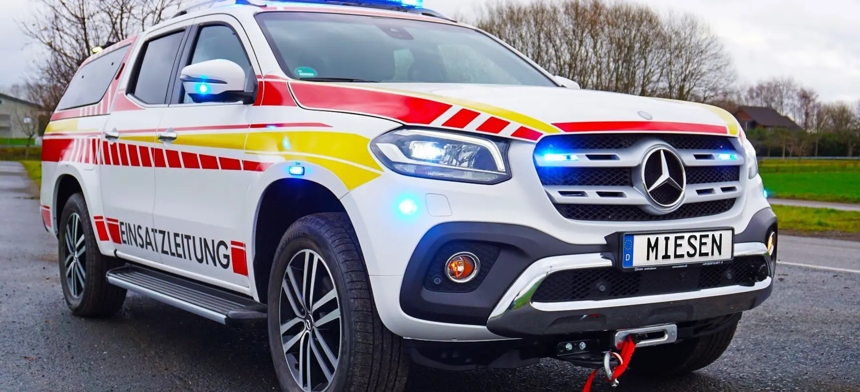 Einsatzleitfahrzeug auf Mercedes-Basis mit Warnbeklebung und eingeschalteter blauer Signalbeleuchtung.