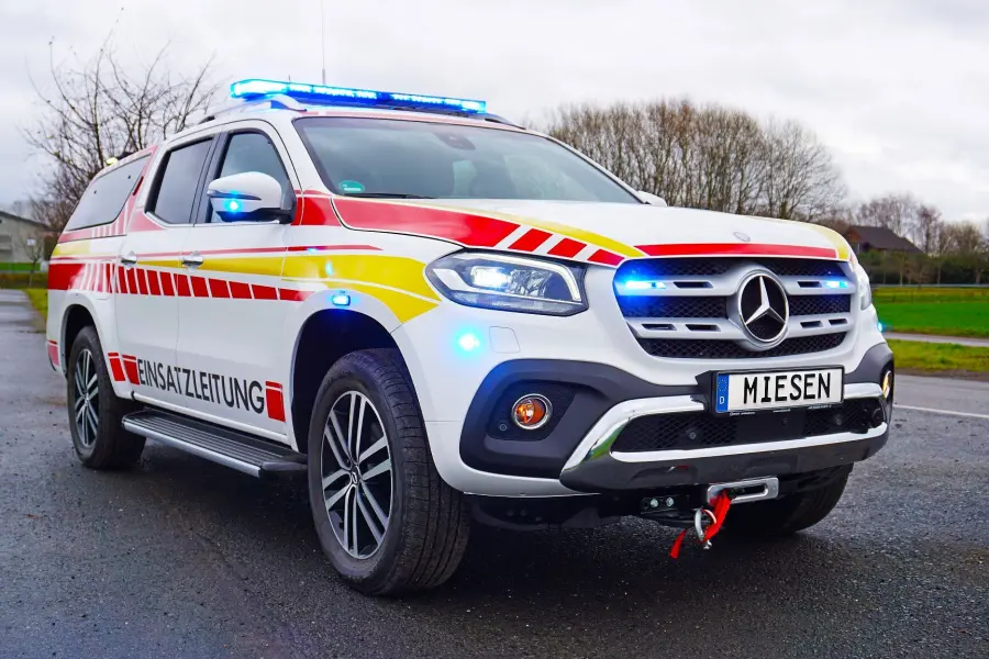 Einsatzleitfahrzeug auf Mercedes-Basis mit Warnbeklebung und eingeschalteter blauer Signalbeleuchtung.